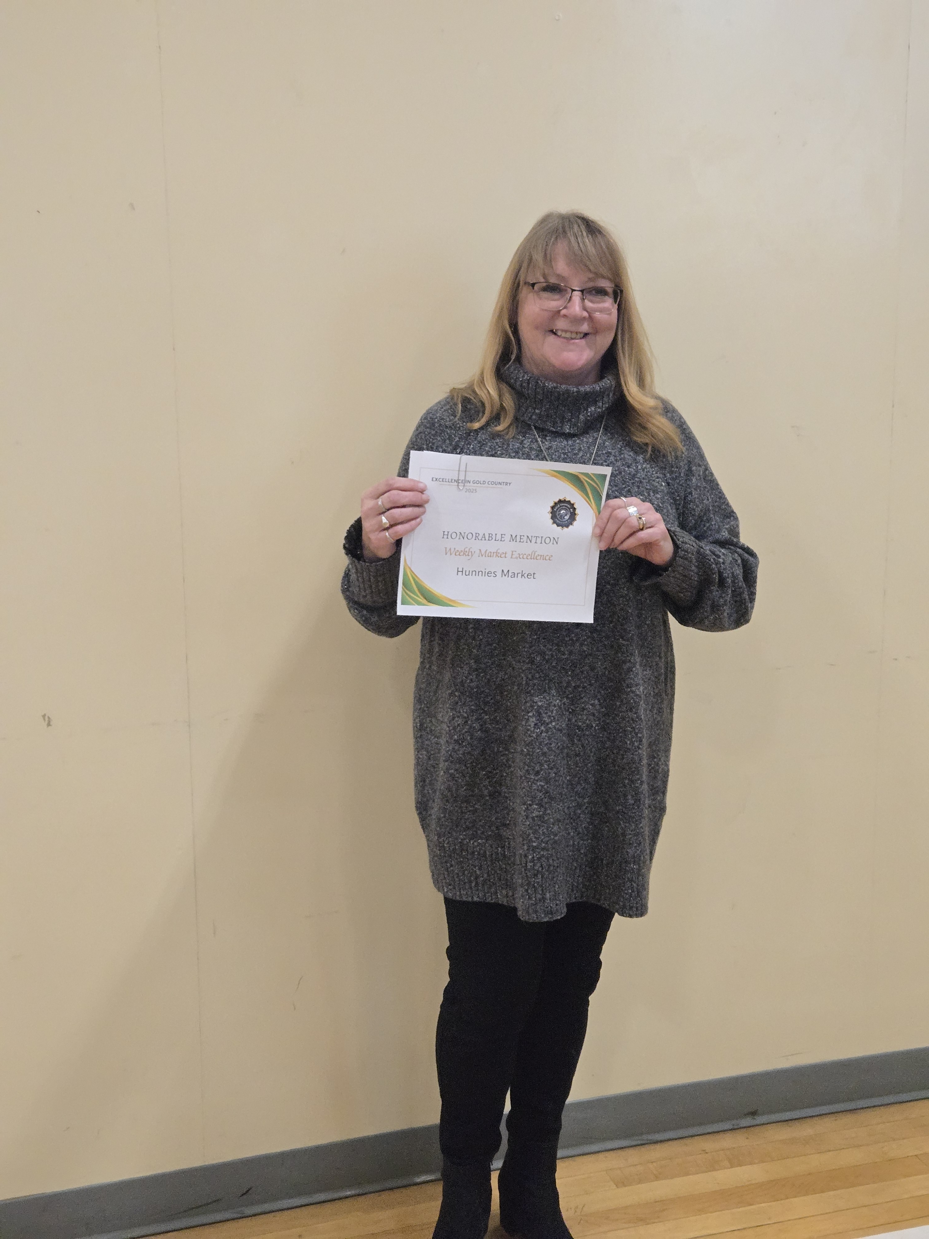 Hunnies Market representative holding an Honourable Mention certificate for Weekly Market Excellence at the Excellence in Gold Country Awards.